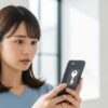 スマートフォンの画面に表示された鍵マークを見て、少し不思議そうな表情を浮かべる若い女性。記事がスマホの謎のアイコン問題を解決することを示唆している。