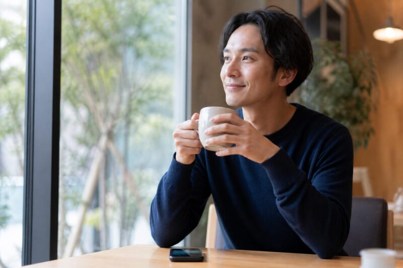 スマホの警告画面を見ても慌てず、温かい飲み物を飲んで落ち着いて対処する男性