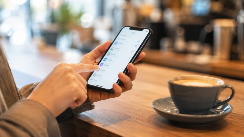カフェで真剣な表情でスマホの設定画面を操作し、RCSオフ設定を進める様子